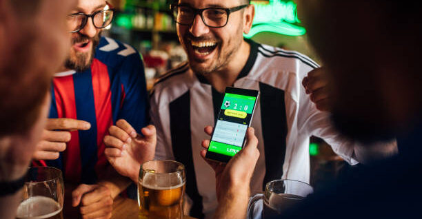Soccer fans drinking beer at the pub and using mobile app for betting.